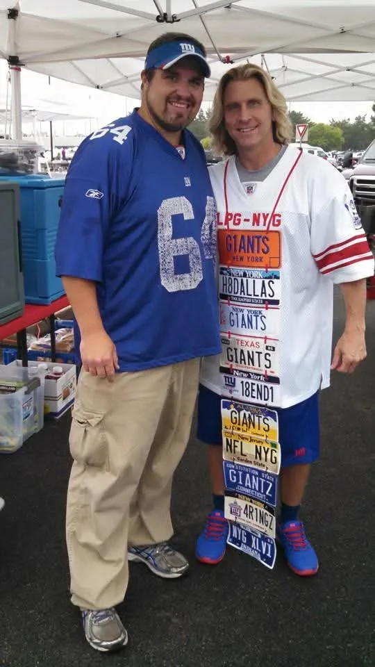 Dan Marney in a blue Giants 64 jersey and visor, posing under a pop-up canopy with a Giants fan wearing a vest of novelty license plates.