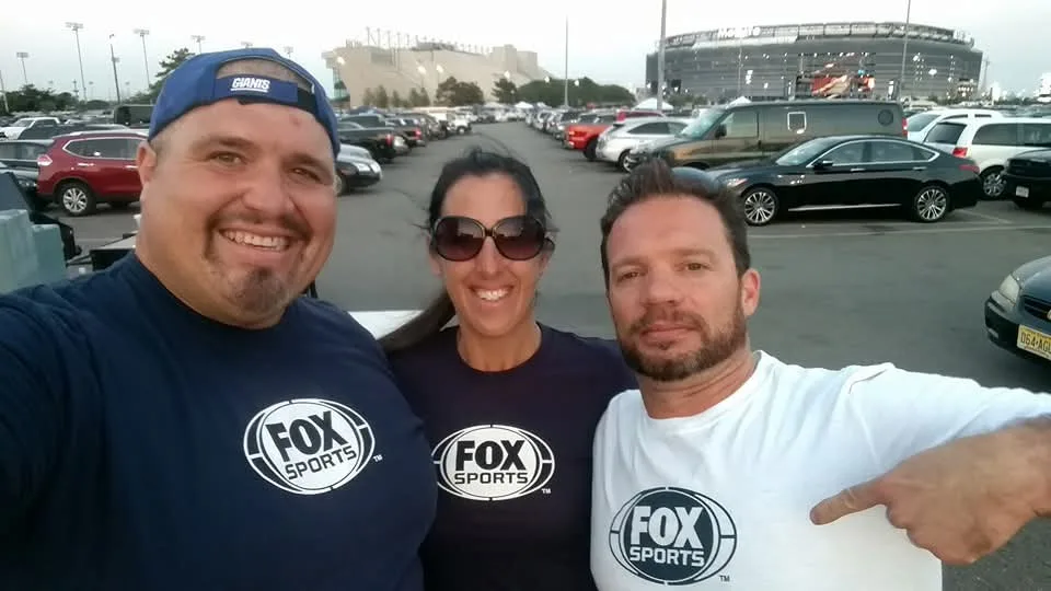 Dan Marney with two others in FOX Sports T-shirts, standing in the parking lot with MetLife Stadium behind them.
